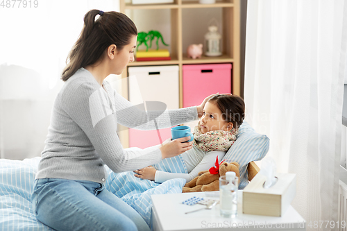 Image of mother giving hot tea to sick little daughter