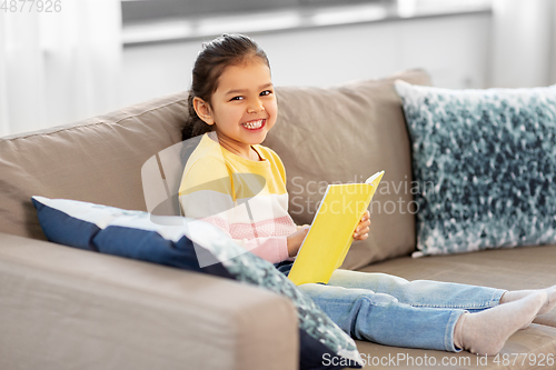 Image of happy smiling little girl reading book at home