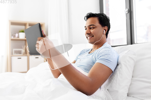 Image of happy indian man with tablet pc in bed at home