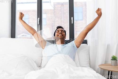 Image of happy smiling indian man lying in bed at home