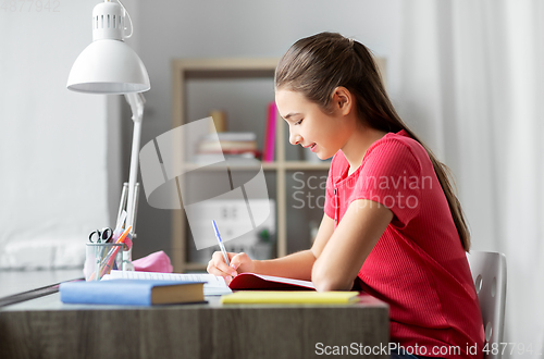 Image of student girl with book writing to notebook at home