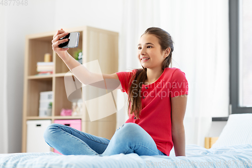 Image of happy girl with smartphone taking selfie at home