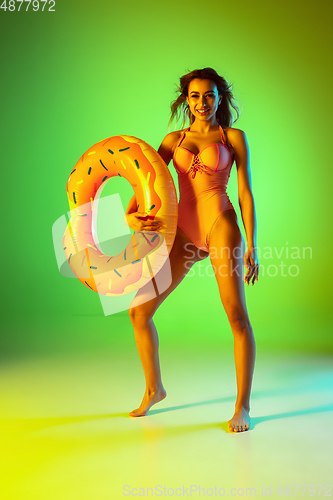 Image of Beautiful girl in fashionable swimsuit isolated on gradient studio background in neon light. Summer, resort, fashion and weekend concept