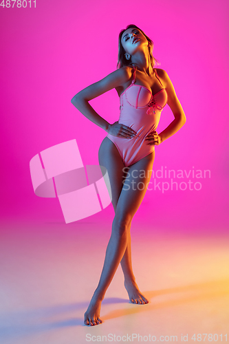 Image of Beautiful girl in fashionable swimsuit isolated on gradient studio background in neon light. Summer, resort, fashion and weekend concept