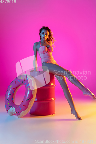 Image of Beautiful girl in fashionable swimsuit isolated on gradient studio background in neon light. Summer, resort, fashion and weekend concept