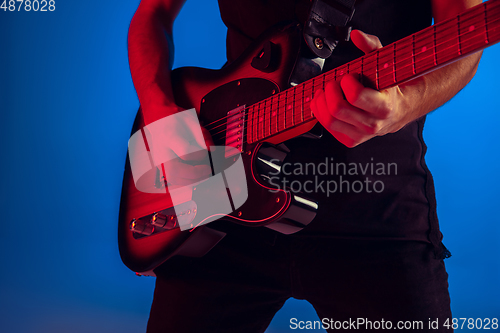 Image of Young caucasian musician playing guitar in neon light on blue background, inspired