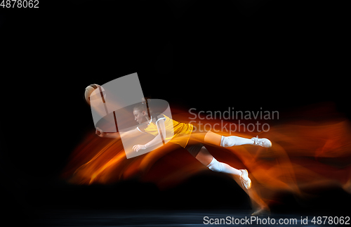 Image of Young female volleyball player isolated on black studio background. Woman in sport\'s equipment training and practicing with fire shadow behind her