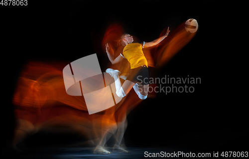 Image of Young female volleyball player isolated on black studio background. Woman in sport\'s equipment training and practicing with fire shadow behind her