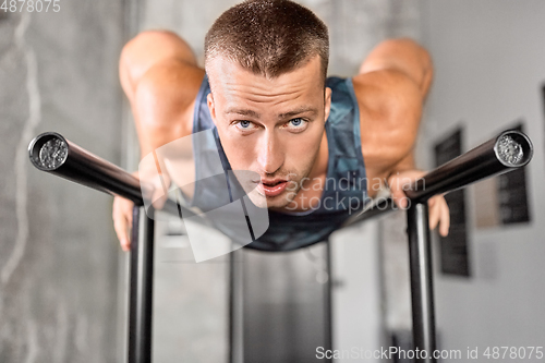 Image of man doing push-ups on parallel bars in gym