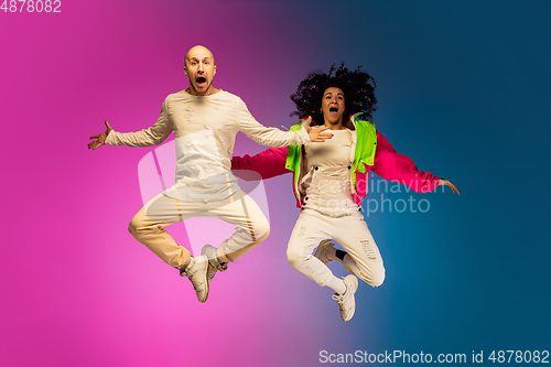 Image of Stylish sportive caucasian couple dancing hip-hop on colorful gradient background at dance hall in neon light.