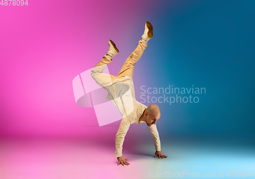 Image of Stylish sportive caucasian man dancing hip-hop on colorful gradient background at dance hall in neon light.