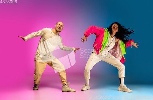 Image of Stylish sportive caucasian couple dancing hip-hop on colorful gradient background at dance hall in neon light.