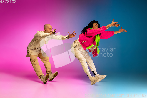 Image of Stylish sportive caucasian couple dancing hip-hop on colorful gradient background at dance hall in neon light.