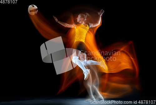 Image of Young female volleyball player isolated on black studio background. Woman in sport\'s equipment training and practicing with fire shadow behind her