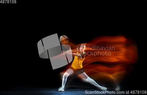 Image of Young female volleyball player isolated on black studio background. Woman in sport\'s equipment training and practicing with fire shadow behind her