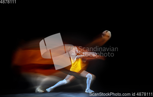 Image of Young female volleyball player isolated on black studio background. Woman in sport\'s equipment training and practicing with fire shadow behind her