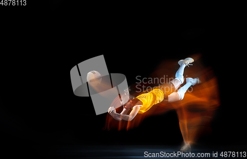 Image of Young female volleyball player isolated on black studio background. Woman in sport\'s equipment training and practicing with fire shadow behind her