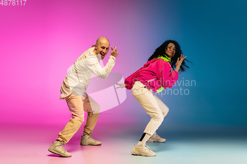 Image of Stylish sportive caucasian couple dancing hip-hop on colorful gradient background at dance hall in neon light.