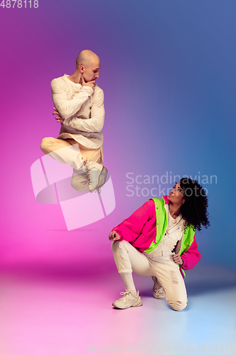 Image of Stylish sportive caucasian couple dancing hip-hop on colorful gradient background at dance hall in neon light.