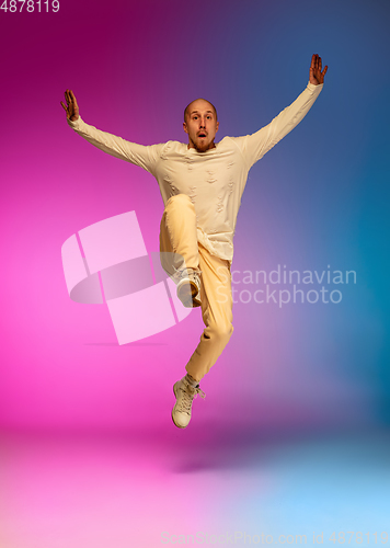 Image of Stylish sportive caucasian man dancing hip-hop on colorful gradient background at dance hall in neon light.