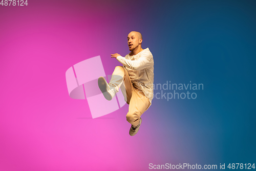 Image of Stylish sportive caucasian man dancing hip-hop on colorful gradient background at dance hall in neon light.