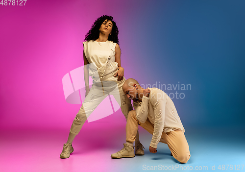 Image of Stylish sportive caucasian couple dancing hip-hop on colorful gradient background at dance hall in neon light.