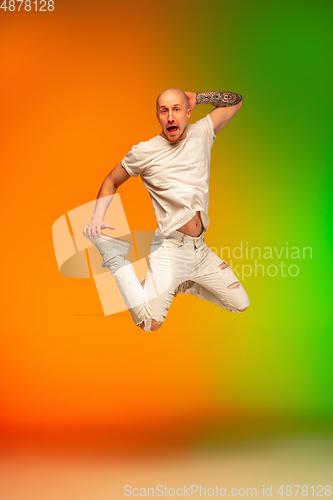 Image of Stylish sportive caucasian man dancing hip-hop on colorful gradient background at dance hall in neon light.