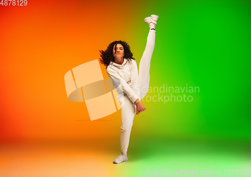 Image of Stylish sportive caucasian woman dancing hip-hop on colorful gradient background at dance hall in neon light.