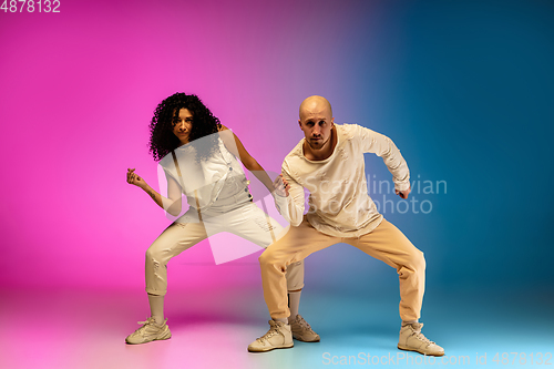 Image of Stylish sportive caucasian couple dancing hip-hop on colorful gradient background at dance hall in neon light.