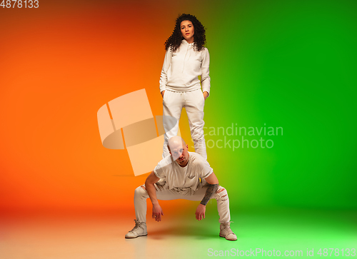 Image of Stylish sportive caucasian couple dancing hip-hop on colorful gradient background at dance hall in neon light.