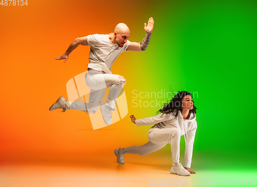 Image of Stylish sportive caucasian couple dancing hip-hop on colorful gradient background at dance hall in neon light.