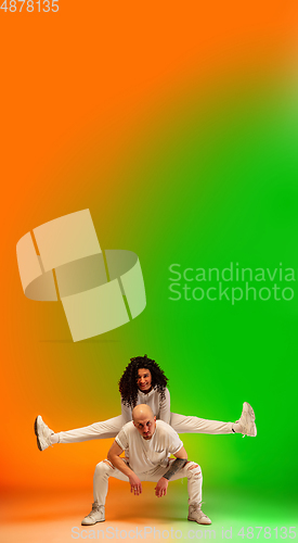 Image of Stylish sportive caucasian couple dancing hip-hop on colorful gradient background at dance hall in neon light.