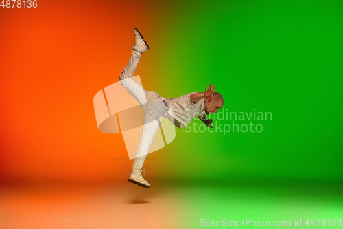 Image of Stylish sportive caucasian man dancing hip-hop on colorful gradient background at dance hall in neon light.