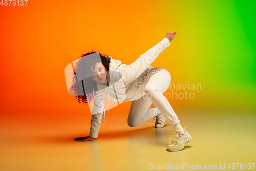 Image of Stylish sportive caucasian woman dancing hip-hop on colorful gradient background at dance hall in neon light.