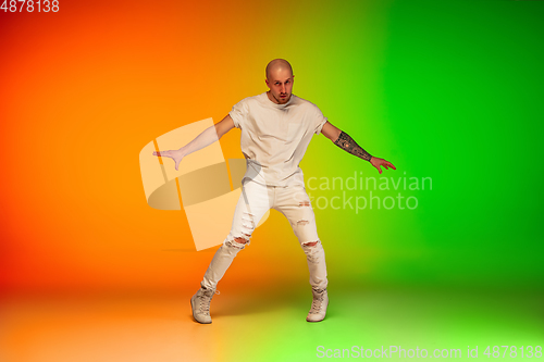 Image of Stylish sportive caucasian man dancing hip-hop on colorful gradient background at dance hall in neon light.