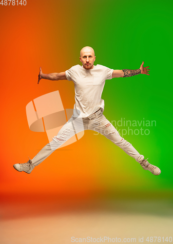 Image of Stylish sportive caucasian man dancing hip-hop on colorful gradient background at dance hall in neon light.