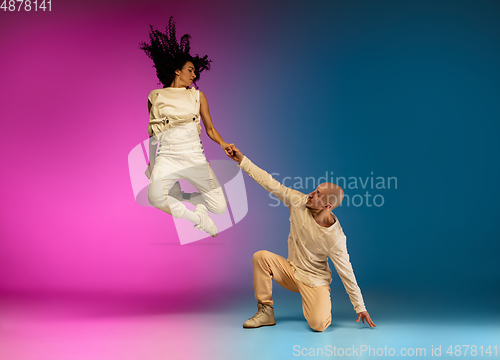 Image of Stylish sportive caucasian couple dancing hip-hop on colorful gradient background at dance hall in neon light.