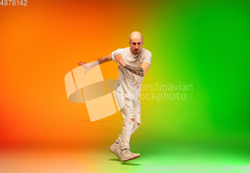 Image of Stylish sportive caucasian man dancing hip-hop on colorful gradient background at dance hall in neon light.