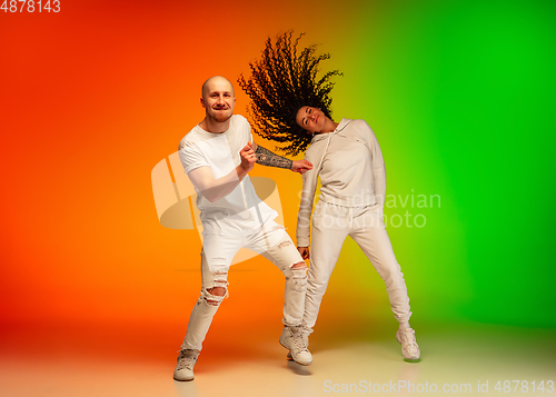 Image of Stylish sportive caucasian couple dancing hip-hop on colorful gradient background at dance hall in neon light.