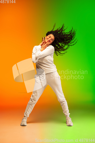 Image of Stylish sportive caucasian woman dancing hip-hop on colorful gradient background at dance hall in neon light.