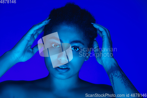 Image of Beautiful african-american woman portrait isolated on blue studio background in neon light, monochrome