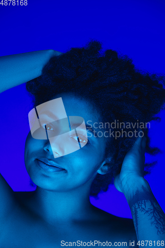 Image of Beautiful african-american woman portrait isolated on blue studio background in neon light, monochrome