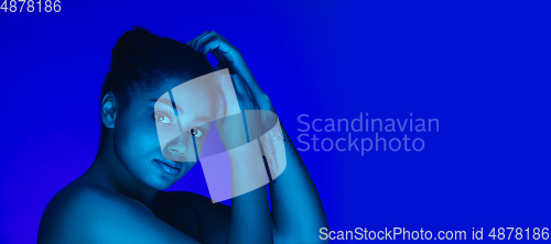 Image of Beautiful african-american woman portrait isolated on blue studio background in neon light, monochrome