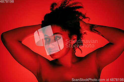 Image of Beautiful african-american woman portrait isolated on red studio background in neon light, monochrome