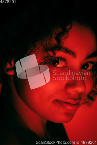 Image of Beautiful african-american woman portrait isolated on red studio background in neon light, monochrome