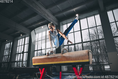 Image of Little male gymnast training in gym, flexible and active. Caucasian fit little boy, athlete in sportswear practicing in exercises for strength, balance.