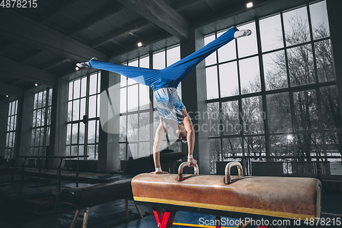 Image of Little male gymnast training in gym, flexible and active. Caucasian fit little boy, athlete in sportswear practicing in exercises for strength, balance.