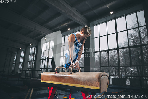 Image of Little male gymnast training in gym, flexible and active. Caucasian fit little boy, athlete in sportswear practicing in exercises for strength, balance.