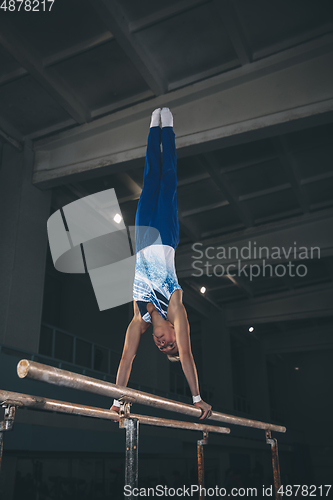 Image of Little male gymnast training in gym, flexible and active. Caucasian fit little boy, athlete in sportswear practicing in exercises for strength, balance.