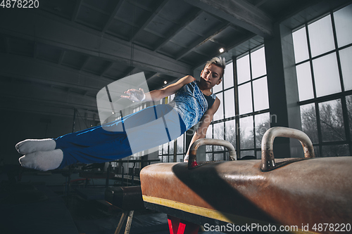 Image of Little male gymnast training in gym, flexible and active. Caucasian fit little boy, athlete in sportswear practicing in exercises for strength, balance.